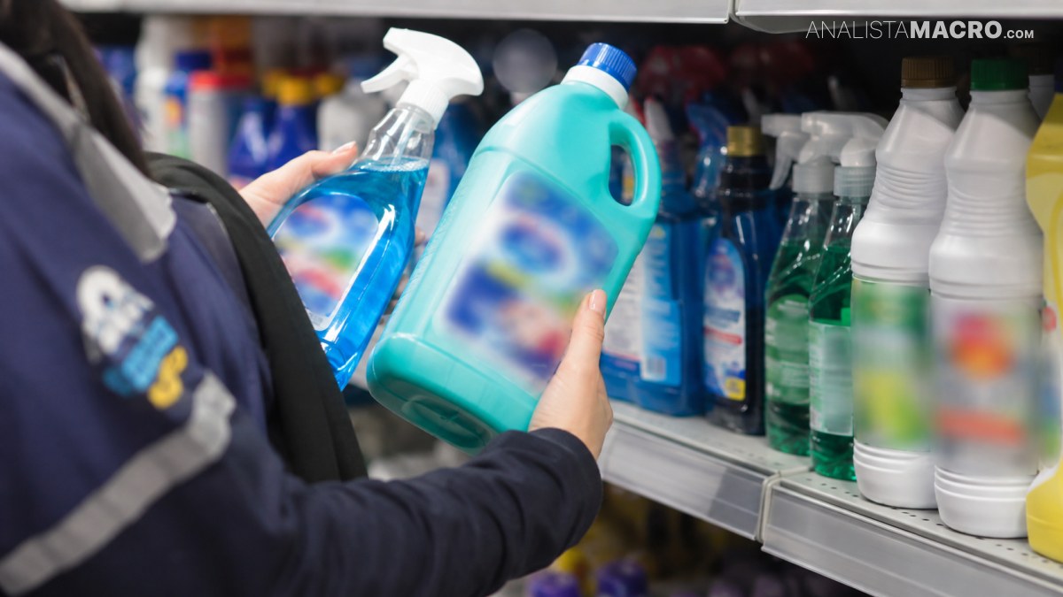 Persona sostiene dos botellas de productos de limpieza frente a un estante con más envases similares.