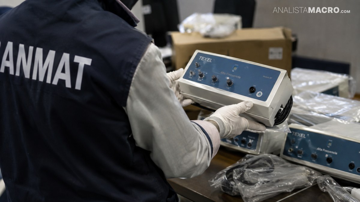 Persona con chaleco oscuro y guantes manipula un dispositivo médico azul sobre una mesa con equipos embalados.