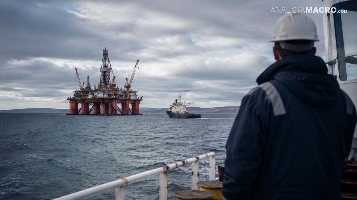 Trabajador con casco observa una plataforma petrolera y un barco en el mar bajo un cielo nublado.