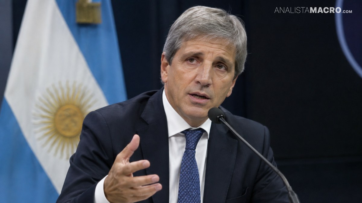 , traje oscuro y corbata azul habla ante un micrófono mientras gesticula, con una bandera argentina detrás.