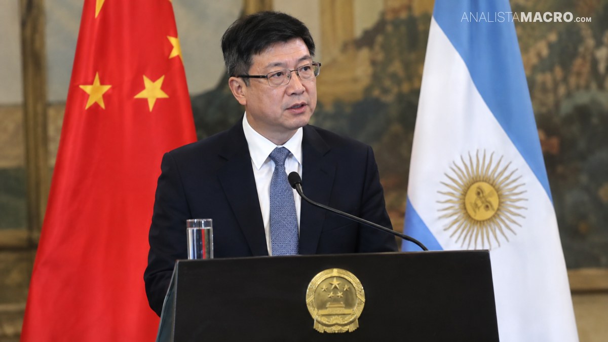 Hombre con gafas y traje oscuro habla ante un atril, flanqueado por las banderas de China y Argentina.
