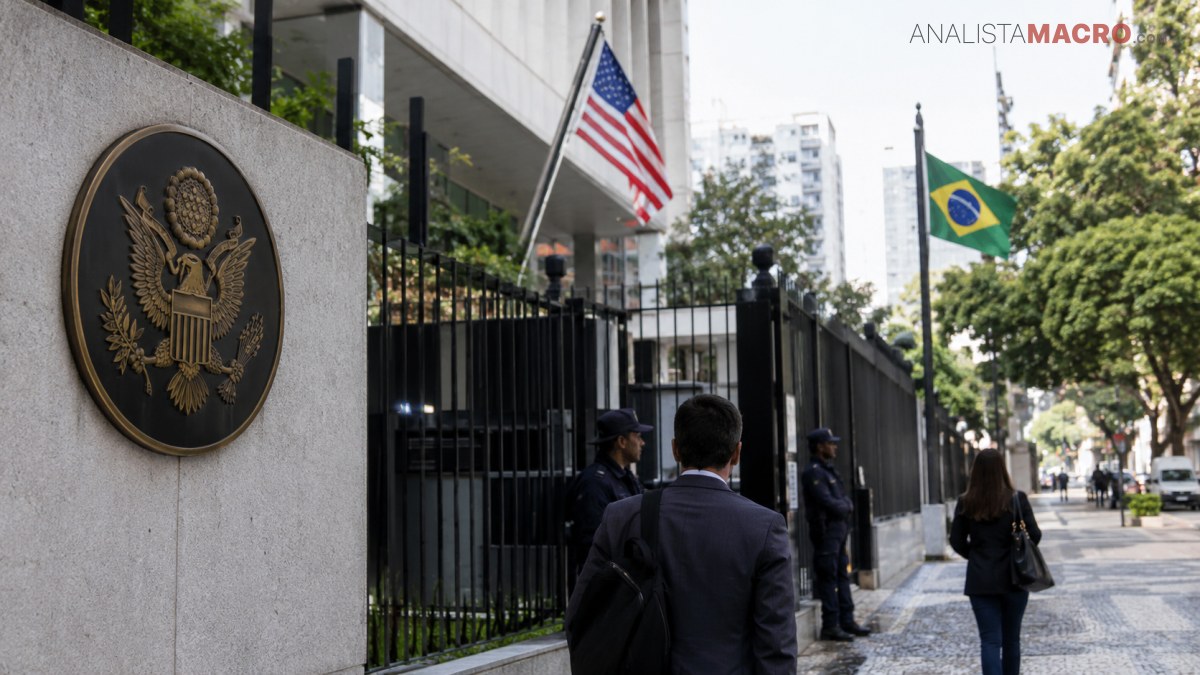 Un edificio cercado exhibe los emblemas de Estados Unidos y Brasil, mientras varias personas caminan por la acera.
