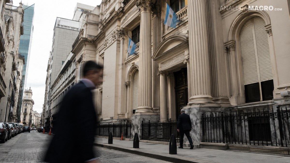 Persona camina frente a un edificio monumental con columnas, banderas azules y una calle urbana bordeada de automóviles.