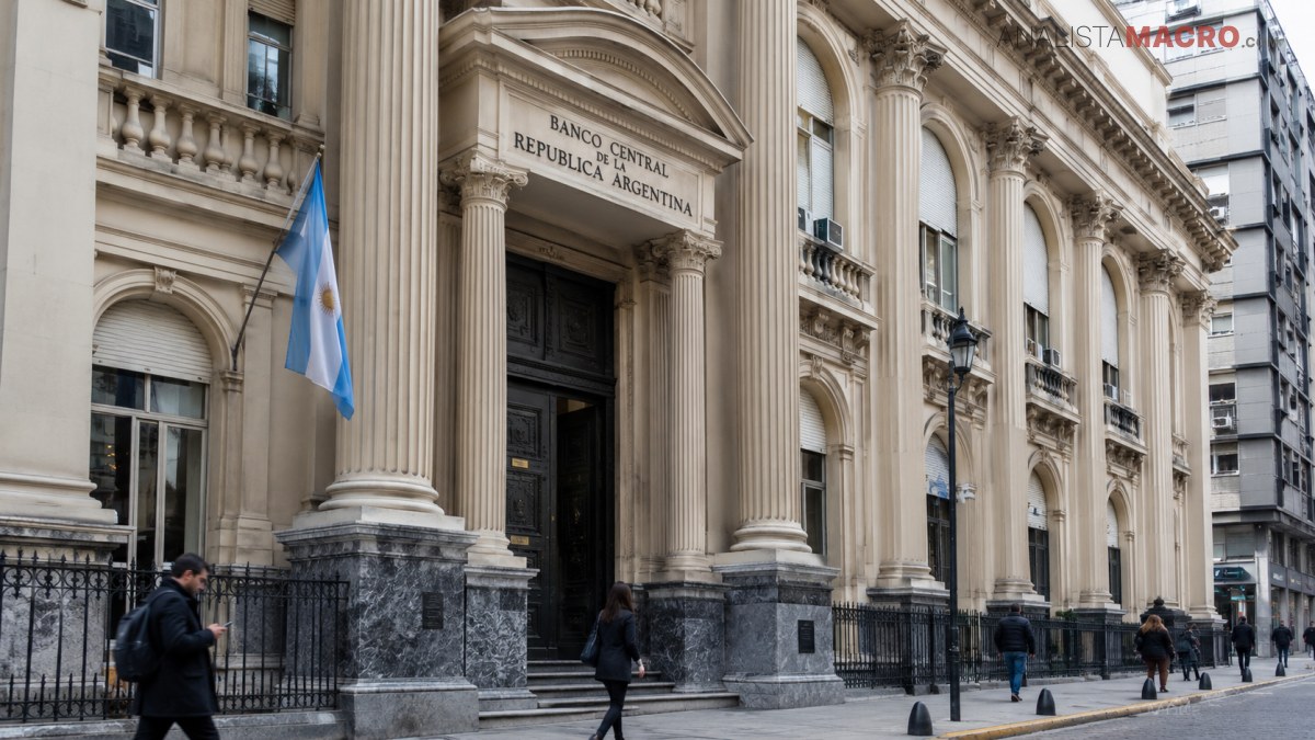Fachada monumental de un banco con columnas, escalinata, bandera argentina y personas caminando frente al edificio.