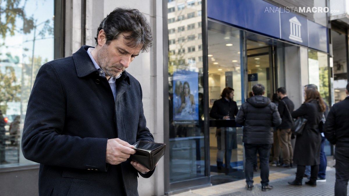Hombre de cabello oscuro revisa su billetera y teléfono frente a la entrada de un edificio, mientras varias personas esperan cerca.