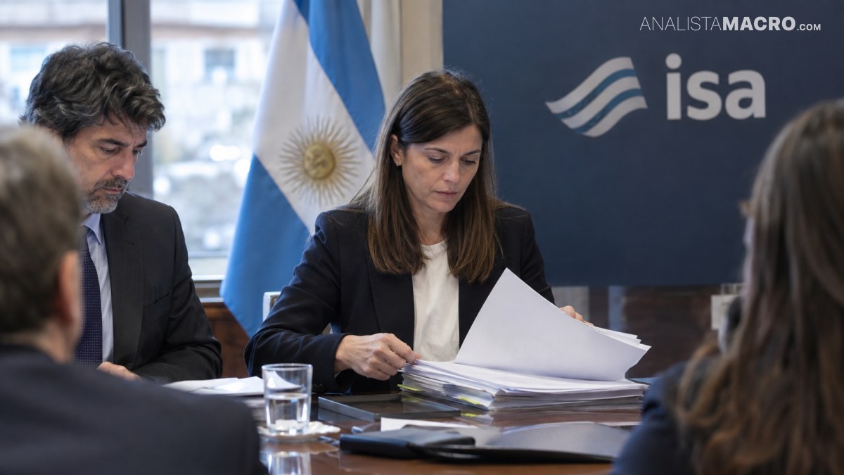 Dos personas revisan documentos en una mesa, junto a una bandera argentina y un cartel con el logotipo de ISA.