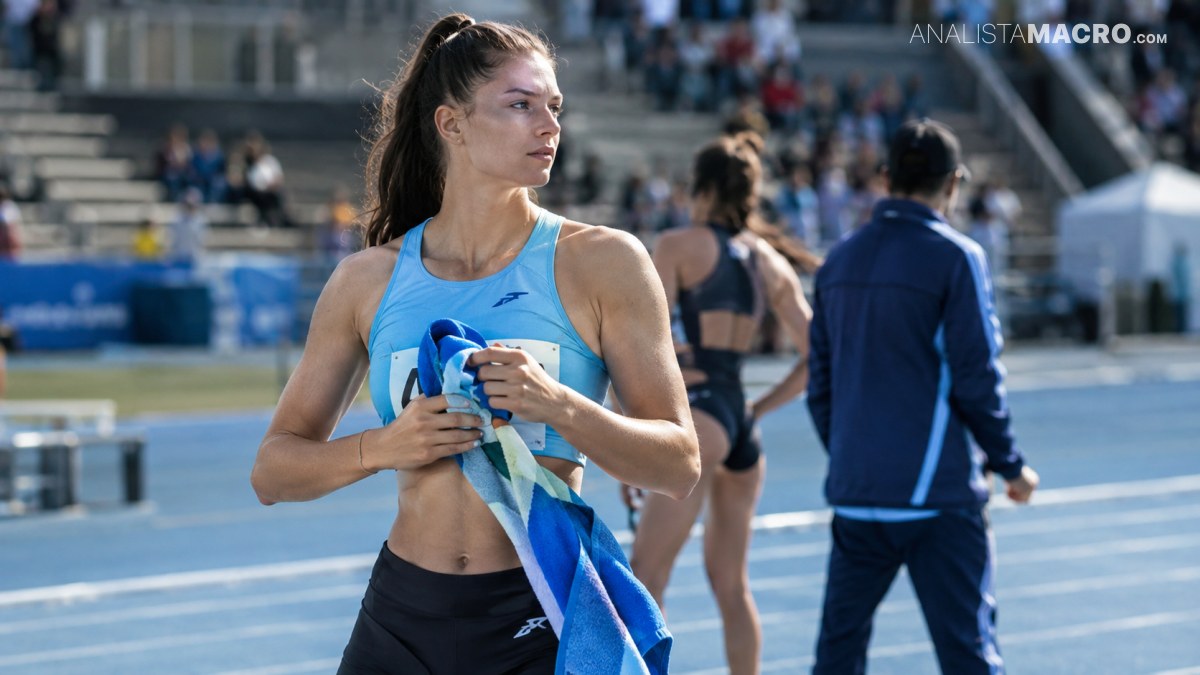 Atleta con camiseta azul sostiene una toalla, mientras varias personas permanecen en una pista al aire libre.