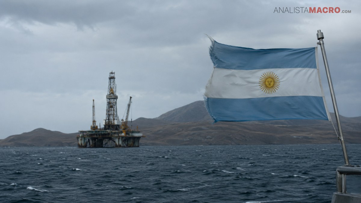 Bandera argentina ondeando en primer plano, con una plataforma petrolera sobre el mar y montañas bajo un cielo nublado.