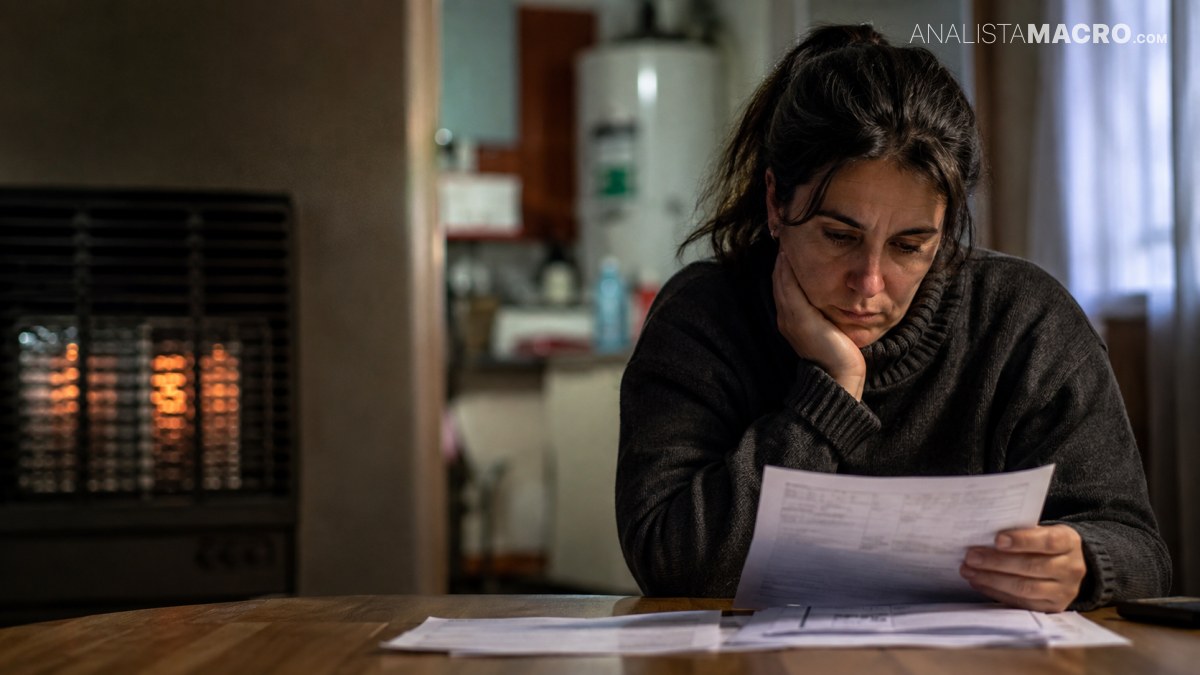 Mujer sentada frente a una mesa, sostiene un documento y se lleva una mano al rostro con expresión preocupada.