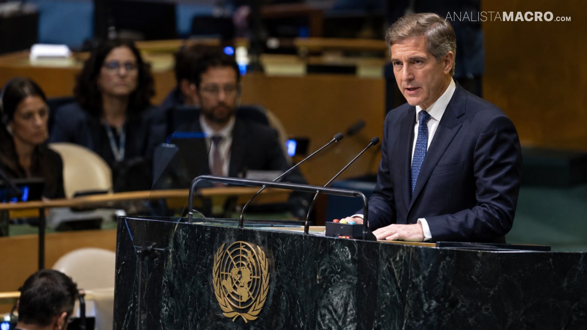 Hombre de traje oscuro habla detrás de un podio con el emblema de la ONU y micrófonos, en una sala con público.
