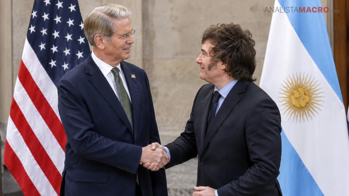 Dos hombres trajeados se estrechan la mano frente a las banderas de Estados Unidos y Argentina.