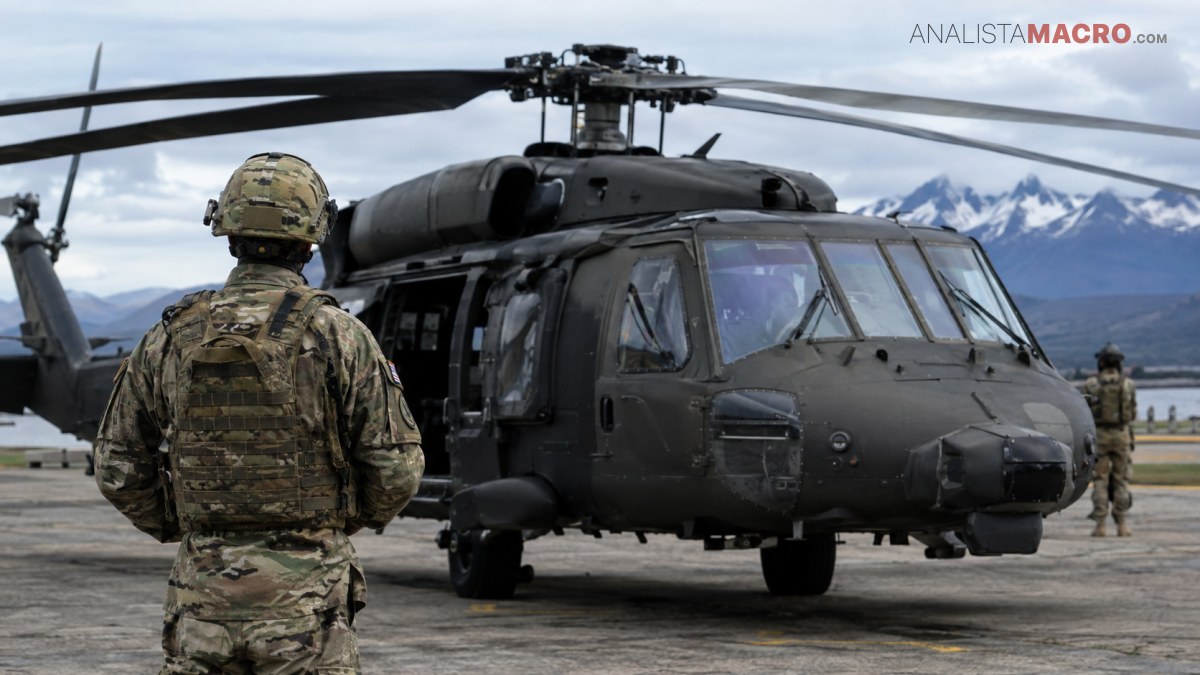Soldado camuflado observa un helicóptero militar negro estacionado en una pista, con montañas nevadas al fondo.