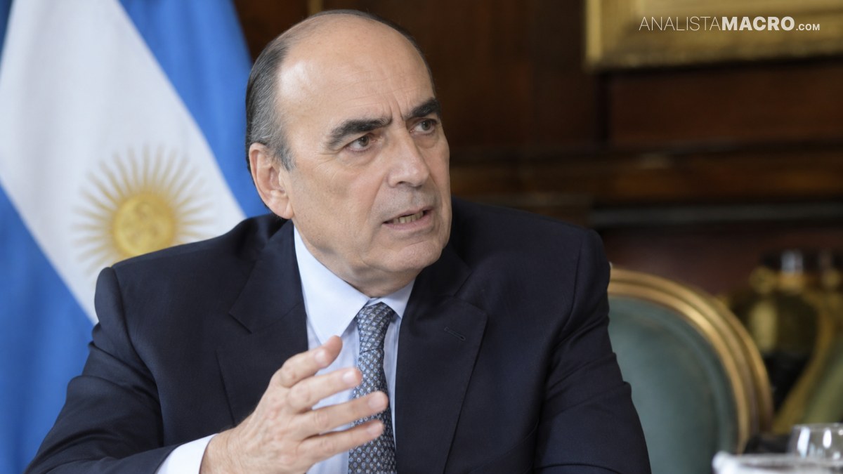 Hombre con traje oscuro y corbata gesticula mientras habla, sentado frente a una bandera argentina y mobiliario de madera.