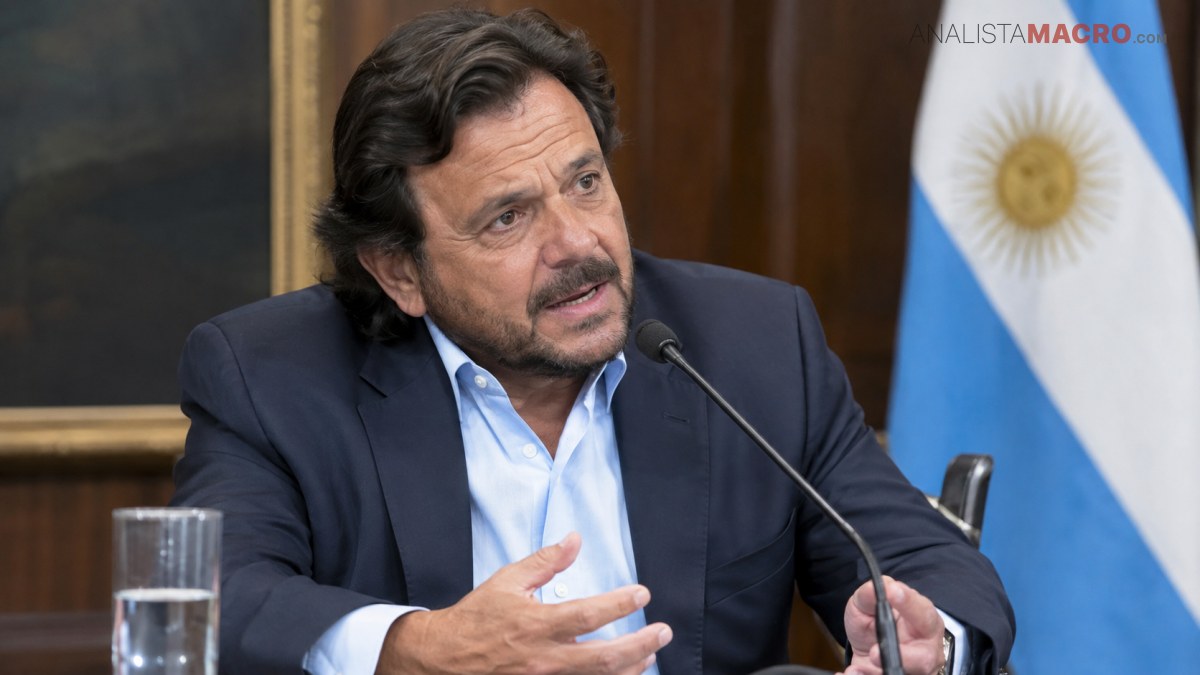 Hombre de cabello oscuro y barba, vestido con traje, habla ante un micrófono junto a una bandera argentina.