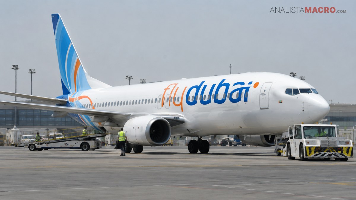 Avión comercial de fuselaje blanco estacionado en una pista, con personal de tierra y vehículos de servicio alrededor.