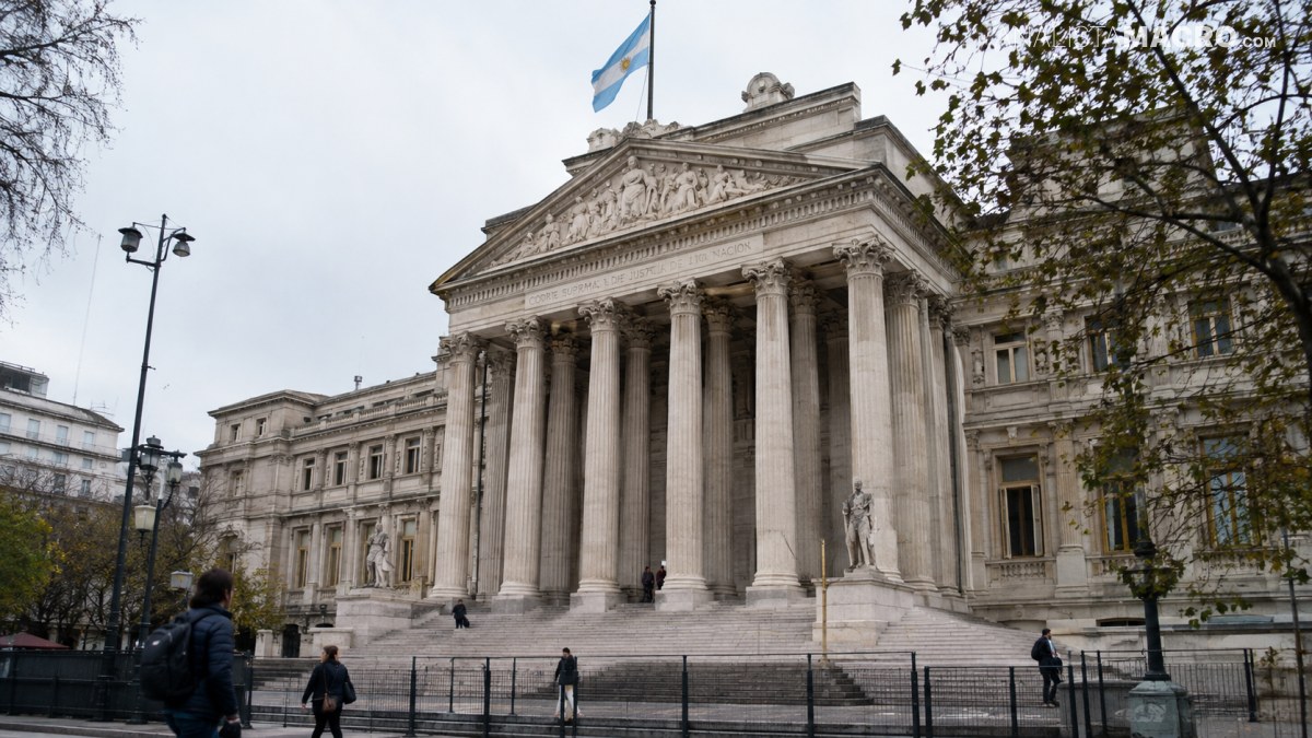 Edificio neoclásico con una amplia escalinata, columnas monumentales, esculturas y una bandera en la parte superior.