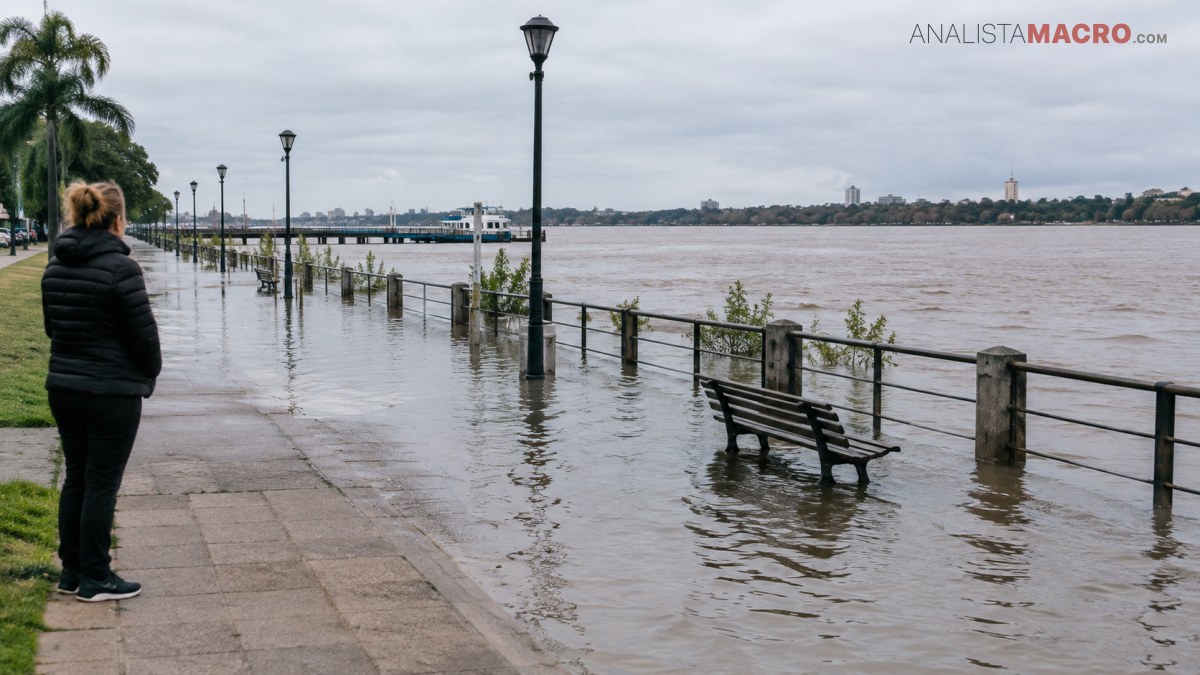 Una mujer observa un paseo costero inundado, con bancos, barandillas y farolas parcialmente sumergidos junto a un río.