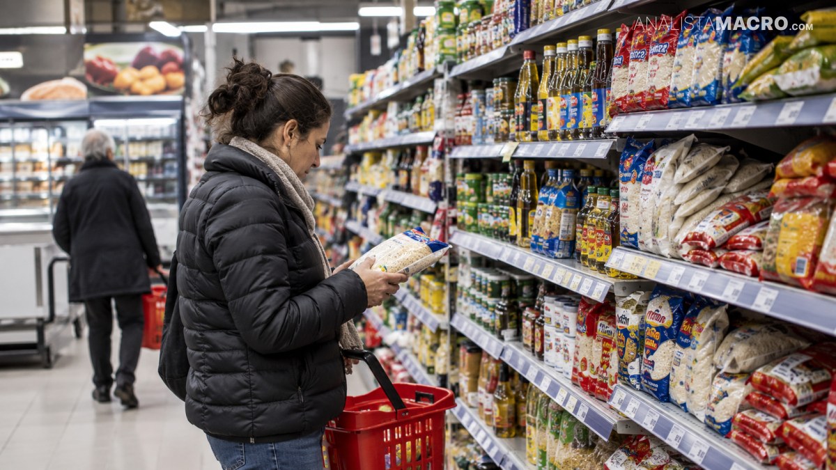 Mujer con abrigo negro revisa un paquete frente a estantes de alimentos mientras sostiene una cesta roja en un supermercado.