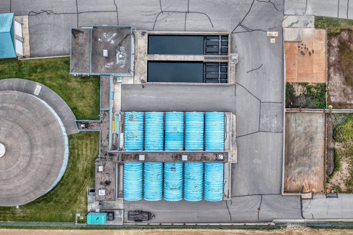 Vista aérea de un complejo industrial con depósitos rectangulares, tubos azules apilados y paredes de hormigón.