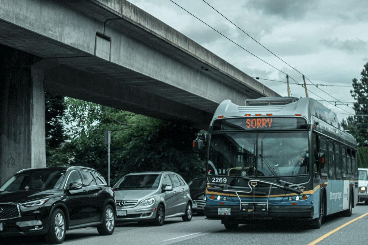 Autobús urbano con letrero “SORRY” se detiene bajo un paso elevado, con coches estacionados alrededor.