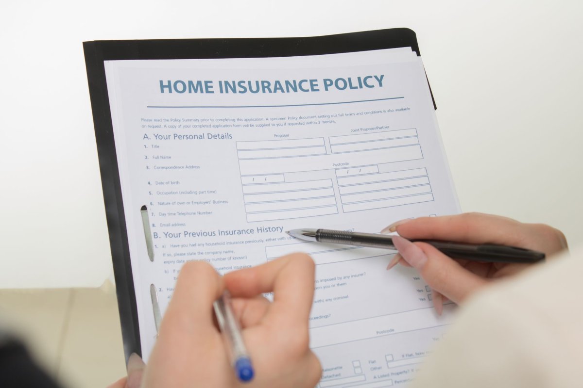 Formulario titulado “HOME INSURANCE POLICY” con espacios para rellenar, sostenido con mano y bolígrafo.