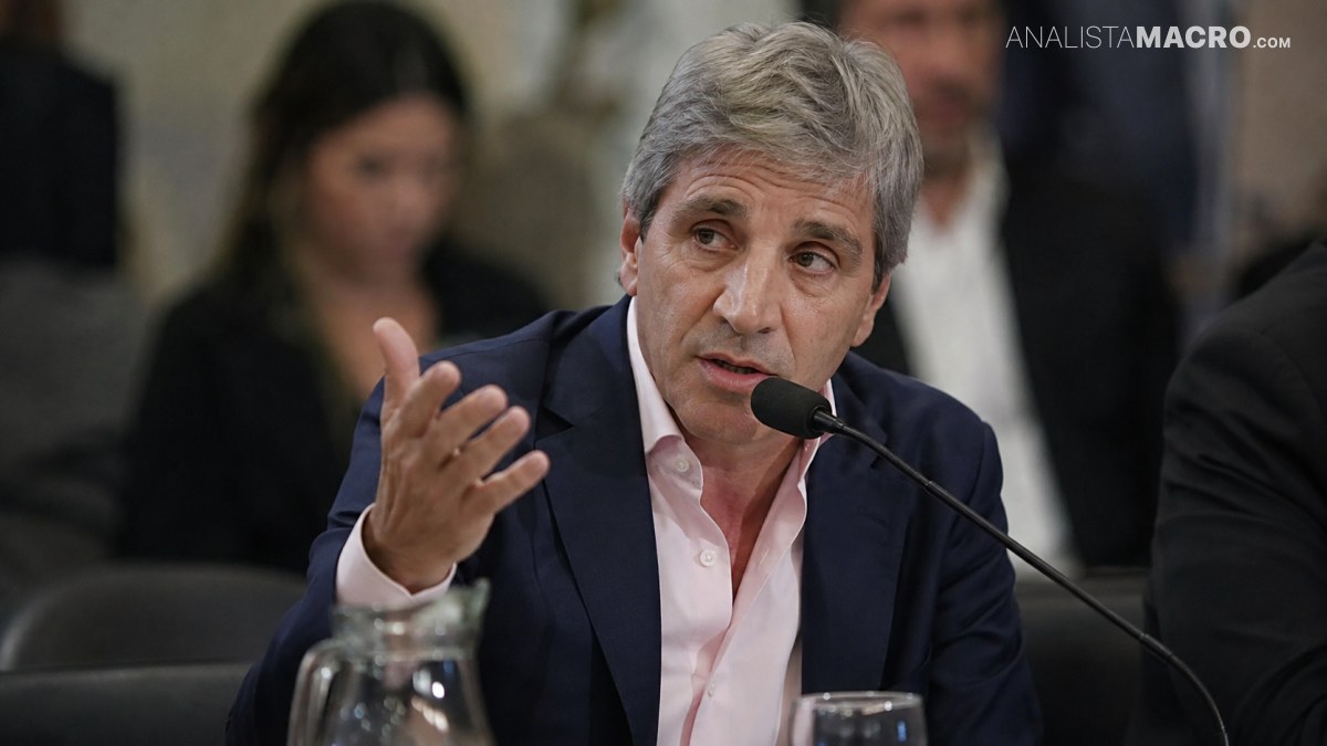 Hombre de cabello canoso habla ante un micrófono, gesticulando con una mano mientras está sentado junto a una mesa.