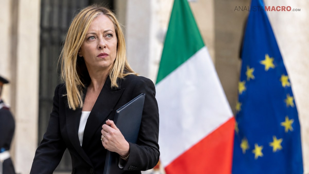 Mujer rubia con traje negro sostiene una carpeta frente a las banderas de Italia y la Unión Europea.