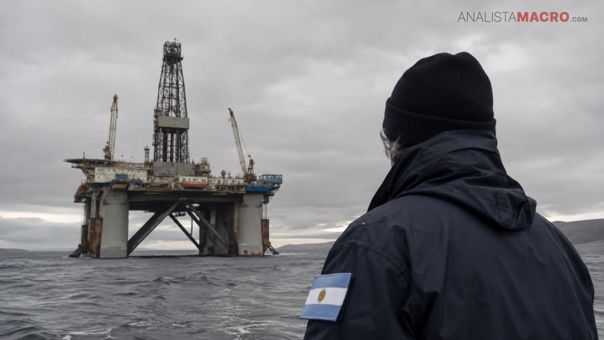 Persona con gorro y chaqueta oscura observa una plataforma petrolera sobre el mar bajo un cielo nublado.