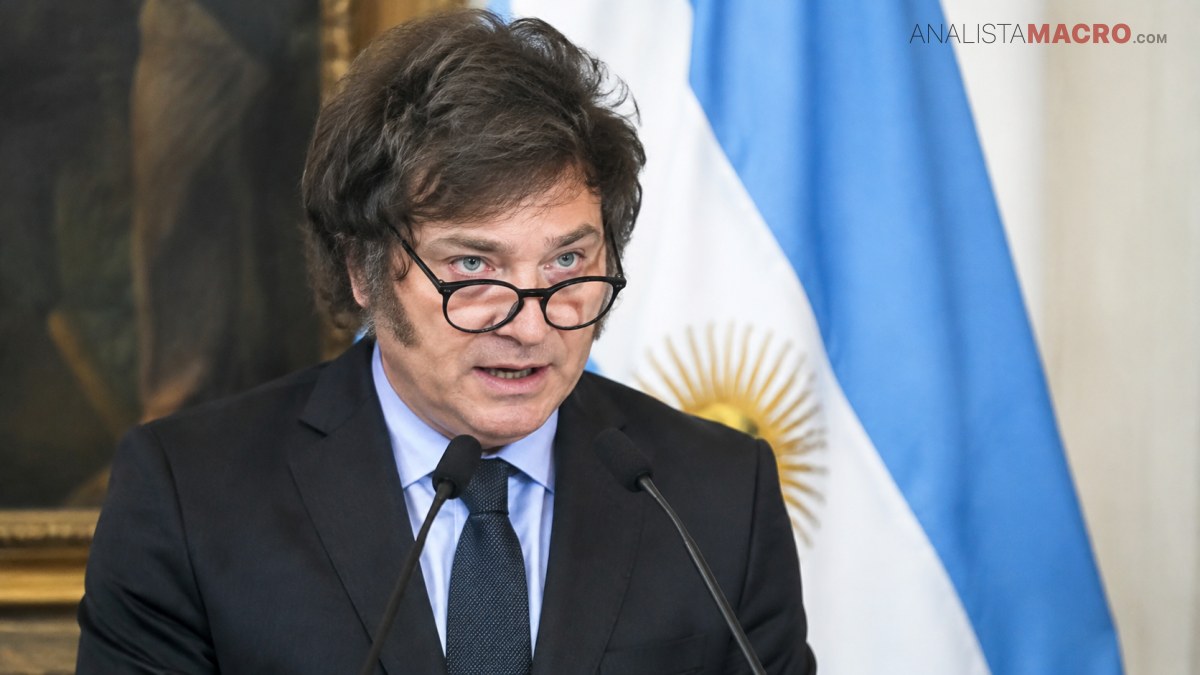 Hombre de cabello oscuro y gafas habla ante dos micrófonos, con una bandera argentina visible al fondo.