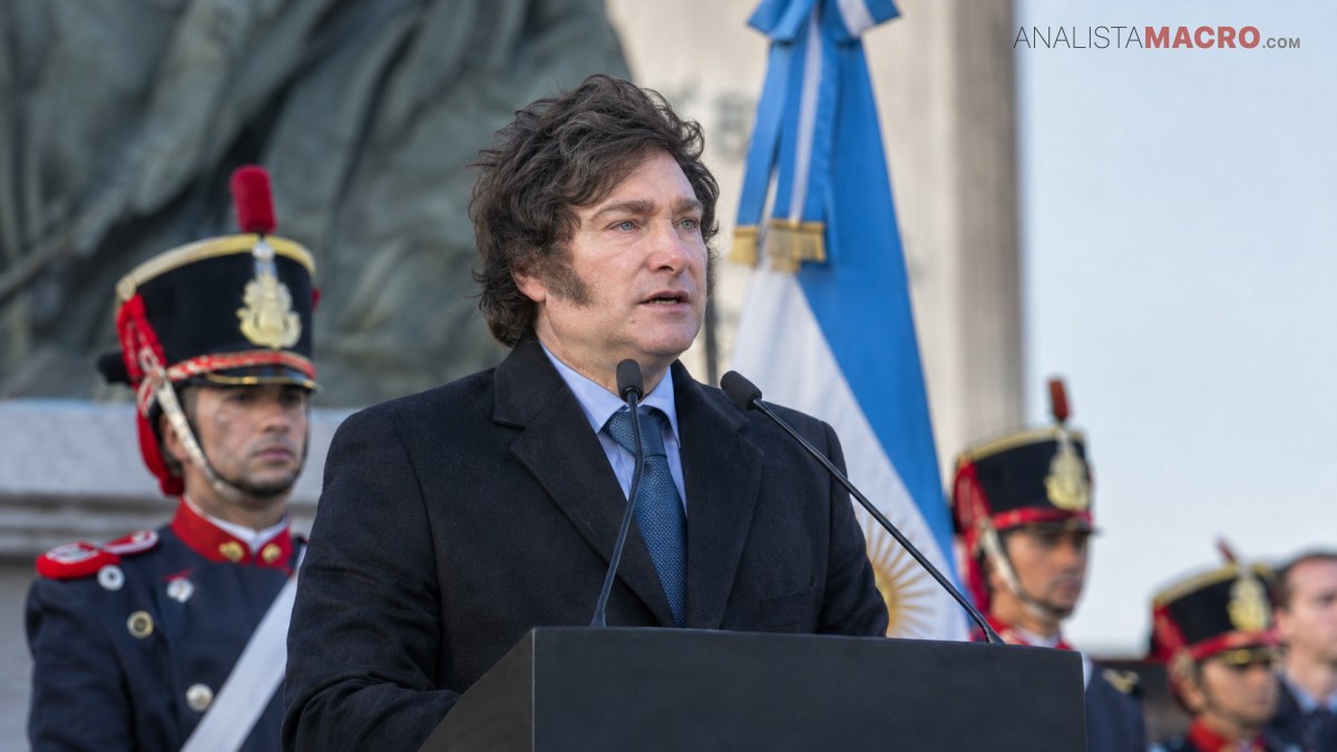 Hombre de cabello oscuro habla ante un podio, acompañado por uniformados y banderas al fondo.