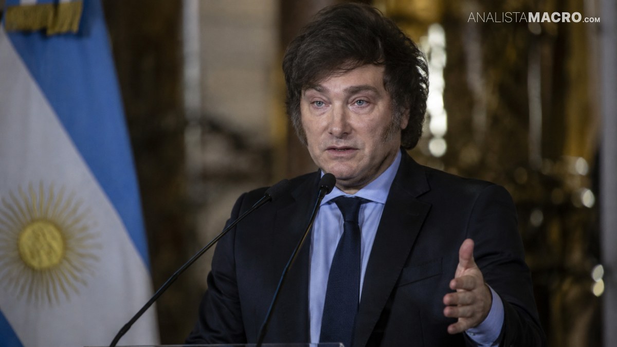 Hombre de cabello oscuro habla ante un micrófono, con traje negro y corbata azul, mientras gesticula con una mano.