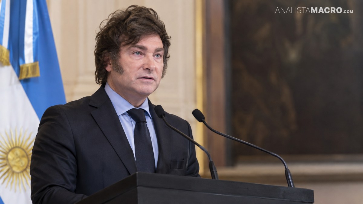 Hombre de cabello oscuro y traje negro habla ante un atril con micrófonos, junto a una bandera argentina.