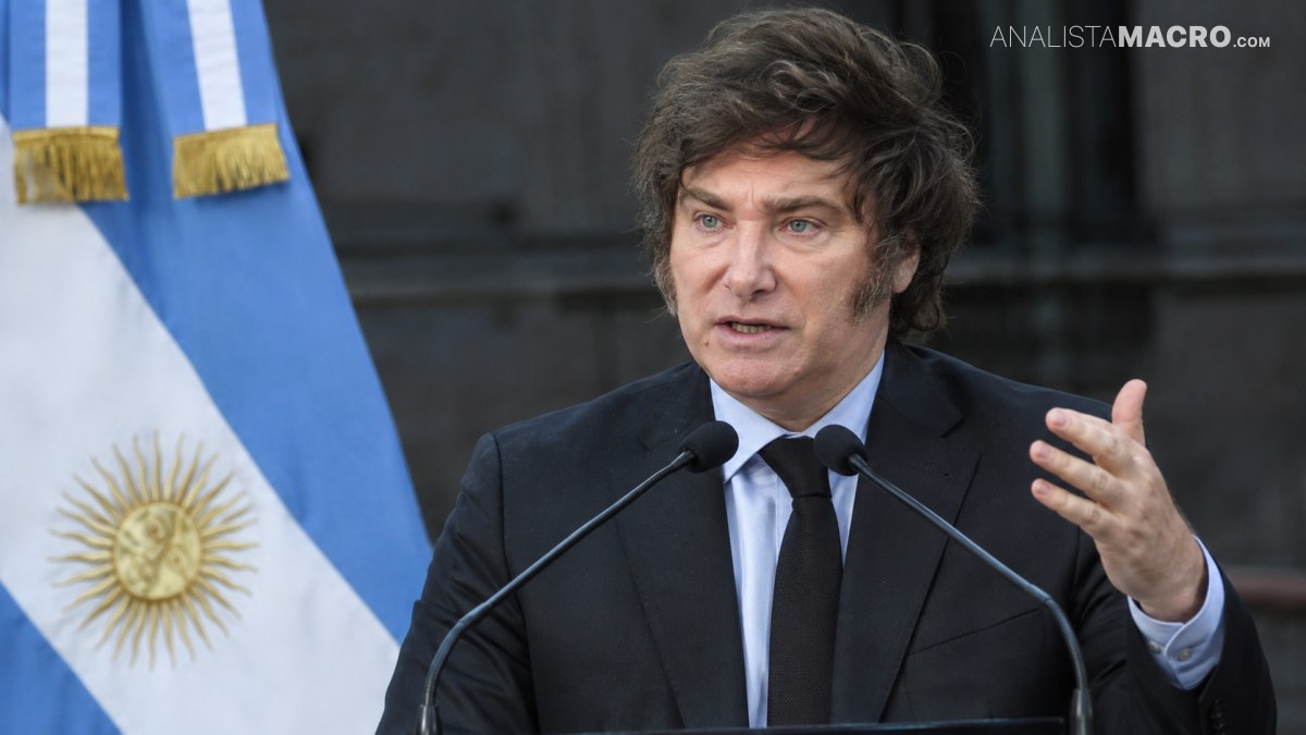 Hombre con traje negro habla en un podio con dos micrófonos, con la bandera argentina al fondo.