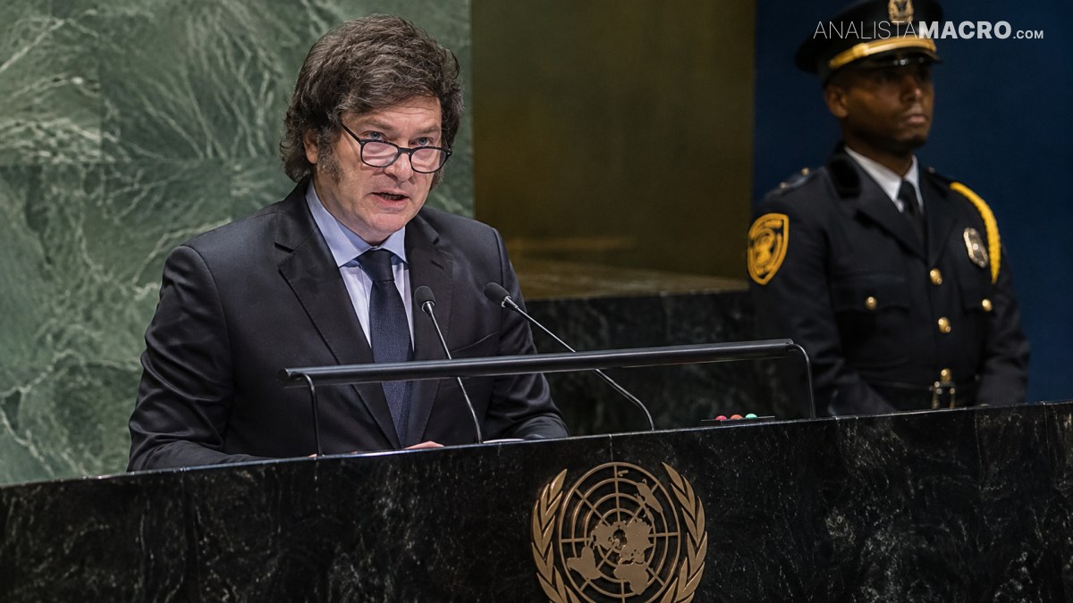 Hombre con traje y gafas habla ante un podio con emblema de las Naciones Unidas, mientras un guardia uniformado permanece detrás.