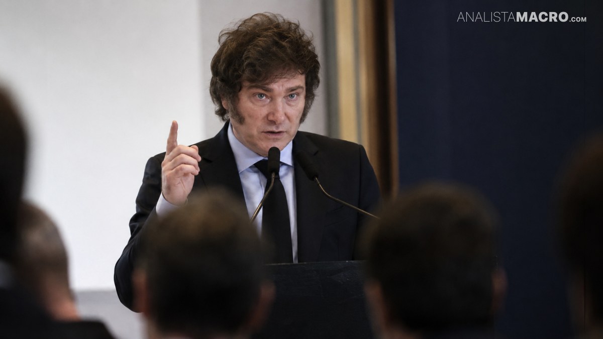 Hombre de cabello rizado, traje oscuro y corbata levanta un dedo mientras habla ante un micrófono.