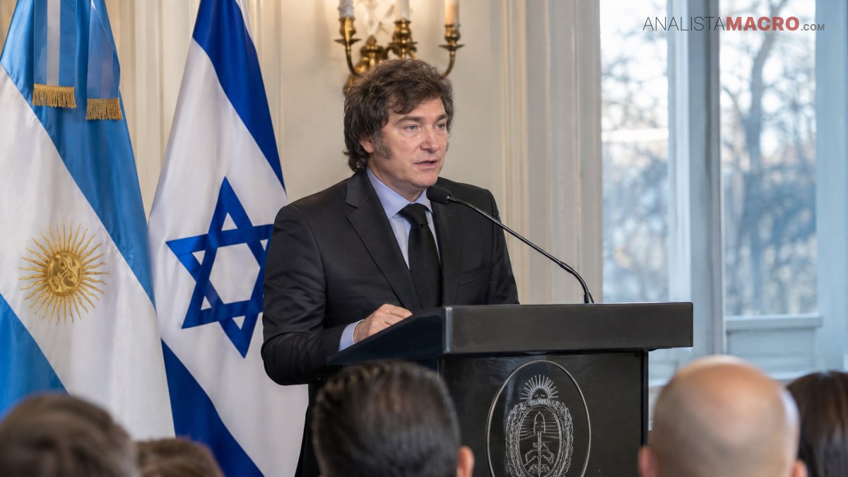 Hombre con traje oscuro habla ante un atril, acompañado por las banderas de Argentina e Israel y varias personas de espaldas.