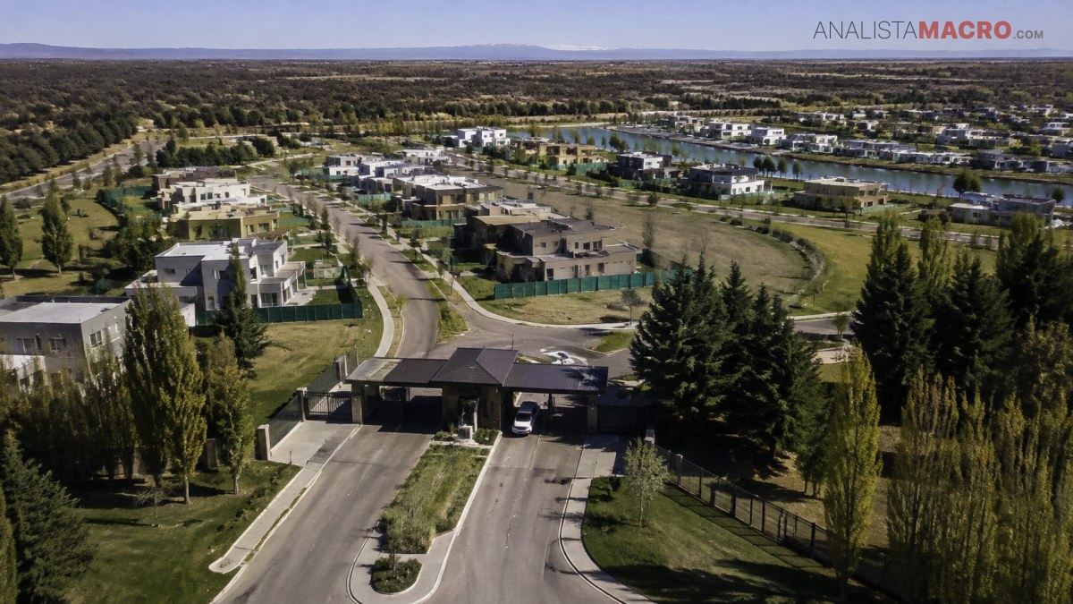 Vista aérea de un complejo residencial con calles, viviendas, áreas verdes y árboles, rodeado de un extenso paisaje urbano.