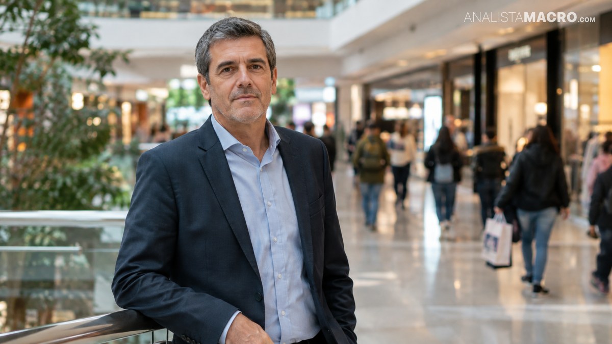 Hombre de cabello canoso, con traje oscuro y camisa azul clara, posa en el interior de un centro comercial.