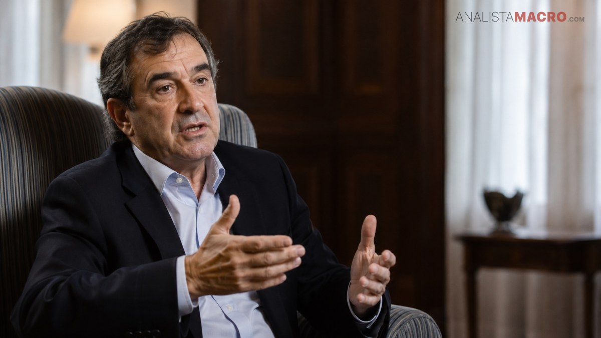 Hombre sentado en un sillón, con traje oscuro, gesticula con ambas manos mientras habla en un interior.
