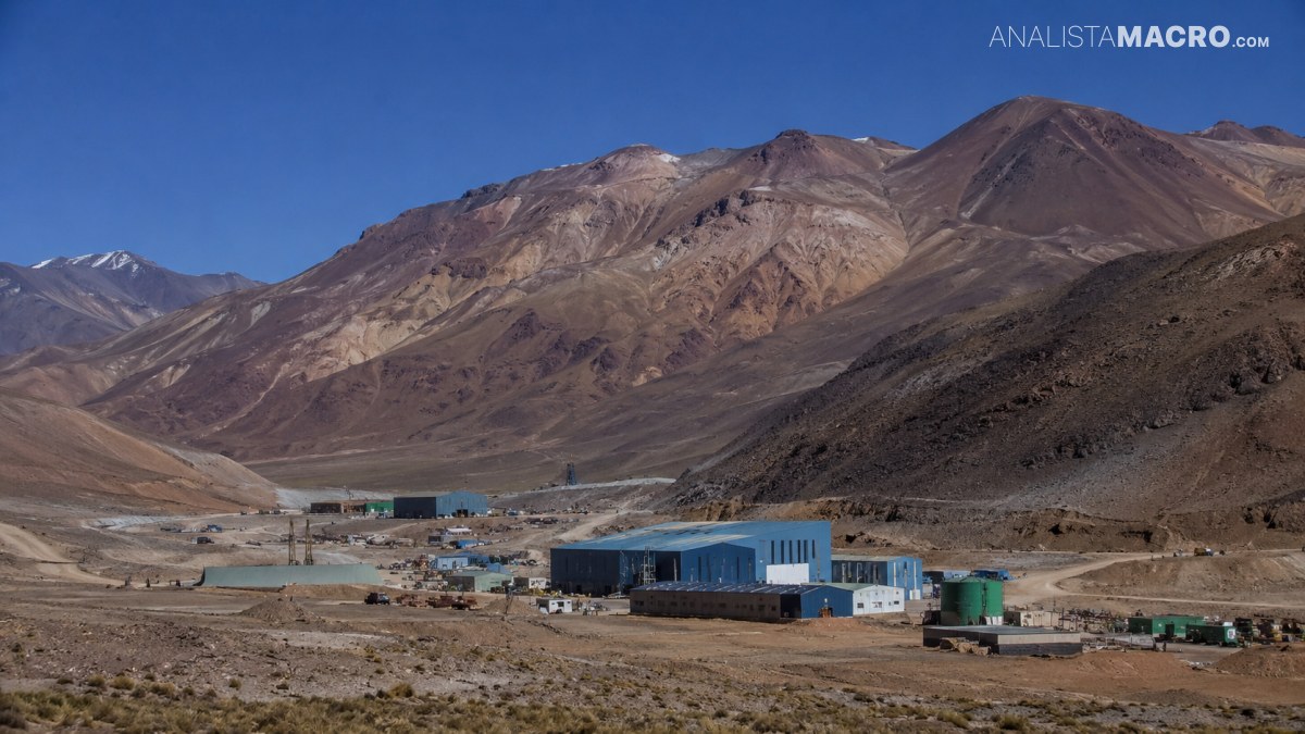 Complejo industrial con edificios azules y vehículos al pie de montañas áridas bajo un cielo despejado.