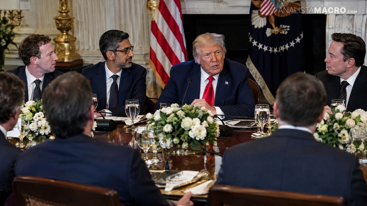 Varias personas conversan alrededor de una mesa formal, con arreglos florales, copas, cubiertos y banderas estadounidenses al fondo.