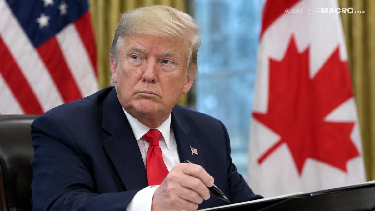 Hombre de cabello rubio sentado, con traje oscuro y corbata roja, sostiene un bolígrafo frente a una carpeta, junto a banderas de Estados Unidos y Canadá.
