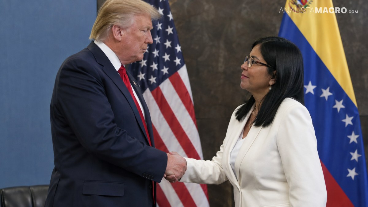 Dos personas con trajes formales se saludan con un apretón de manos frente a banderas de Estados Unidos y Ucrania.
