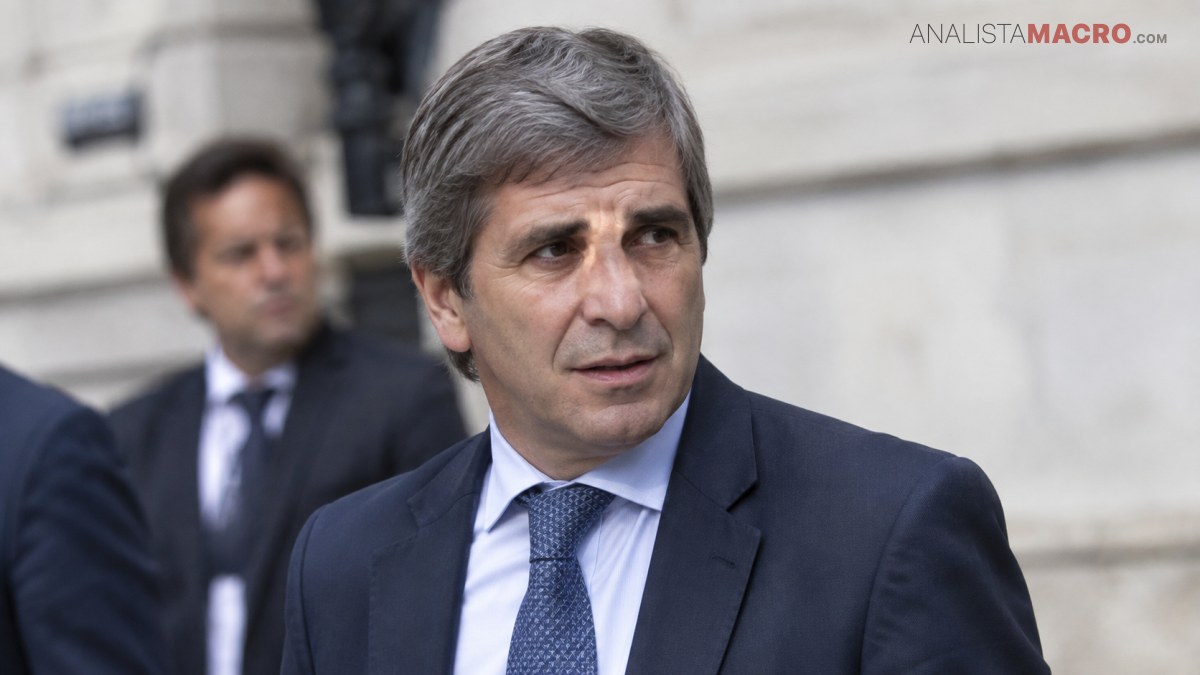Hombre de cabello canoso con traje oscuro y corbata azul, mirando hacia un lado frente a un edificio.